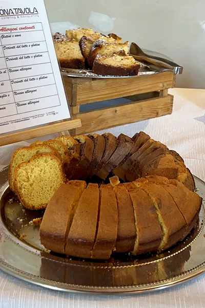 Torta a fette su vassoio con cartello allergeni accanto, esempio di struttura essenziale per IAD home food e catering